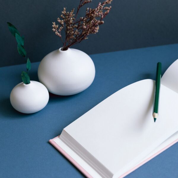 Blank notebook and pencil with vase of dry flowers on desk. navy blue wall background. workspace